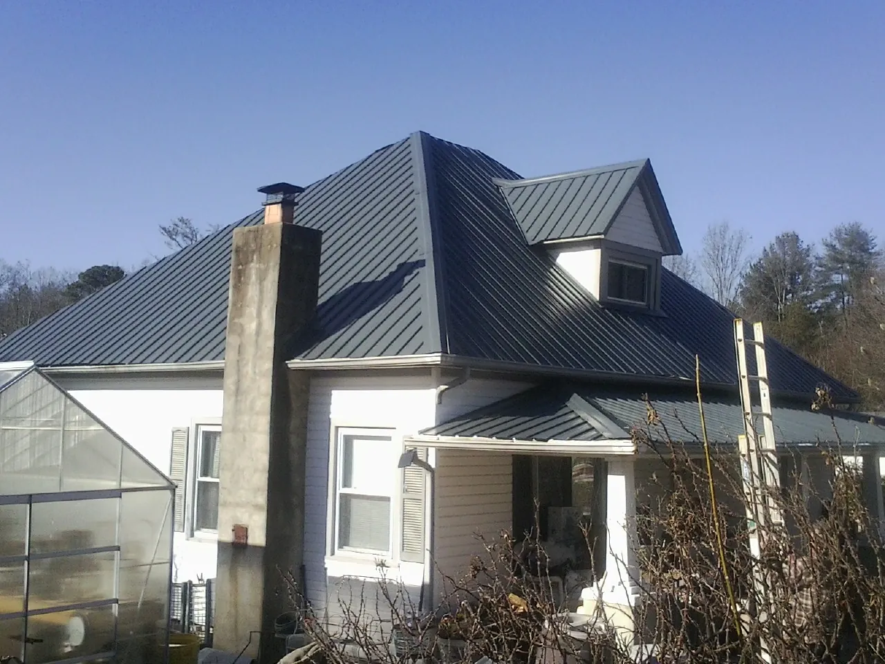 Dark blue standing seam metal roof on a white farmhouse with dormer — Slate & Tile Roof Repair by Roofing Brothers in Elbow Lake
