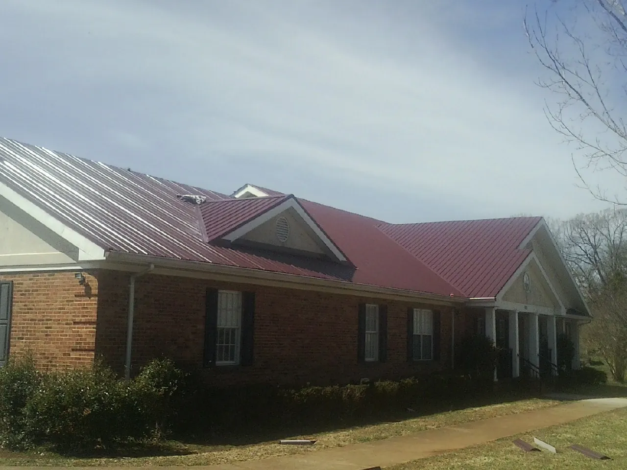 Red metal roof with gabled entries on a long brick building, from a Hail Damage Roof Repair job in Elbow Lake