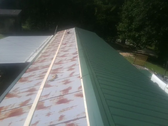 Old rusted panels beside newly installed green metal roofing — Wind Damage Roof Repair by Roofing Brothers in Elbow Lake