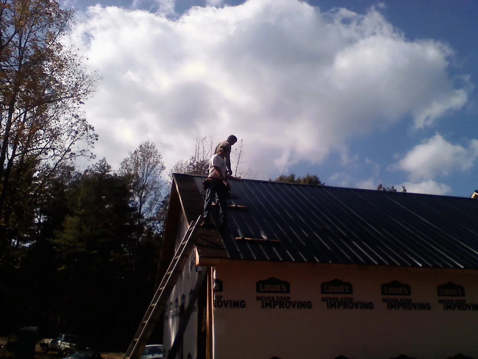 Roofer fastening dark metal panels high against a cloudy sky, from a Roof Inspection job in Elbow Lake