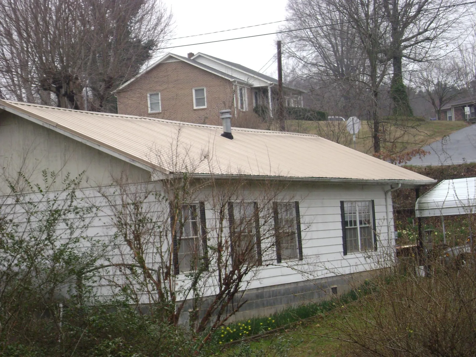 Tan metal roof on a white sided house set into a hillside — Commercial Roofing by Roofing Brothers in Elbow Lake