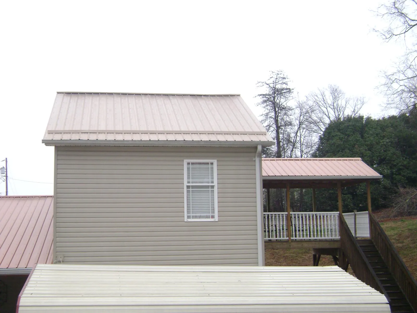 Tan metal roofs on a two story addition and attached porch, from a Roof Replacement job in Elbow Lake
